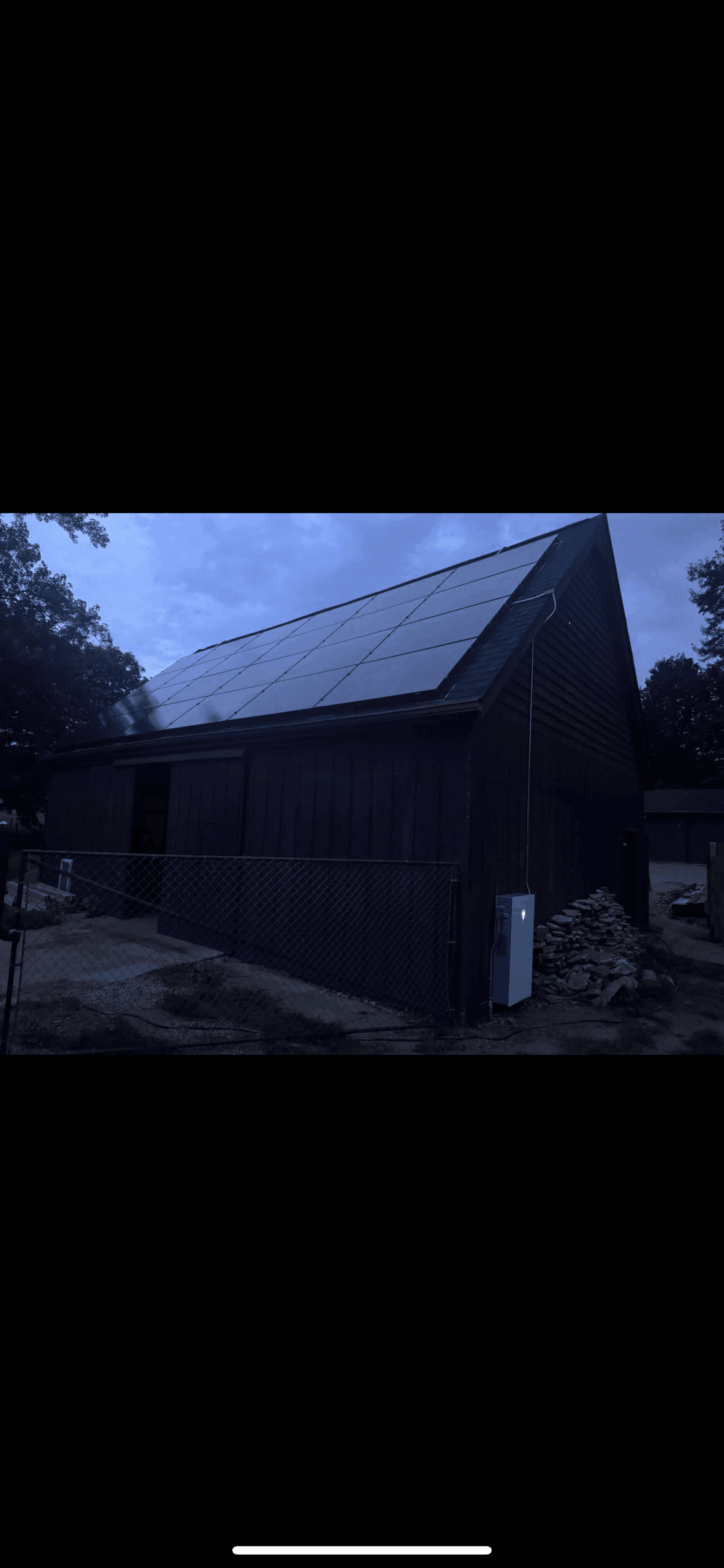 Building with solar panels on steep roof angle with inverter box visible at dusk